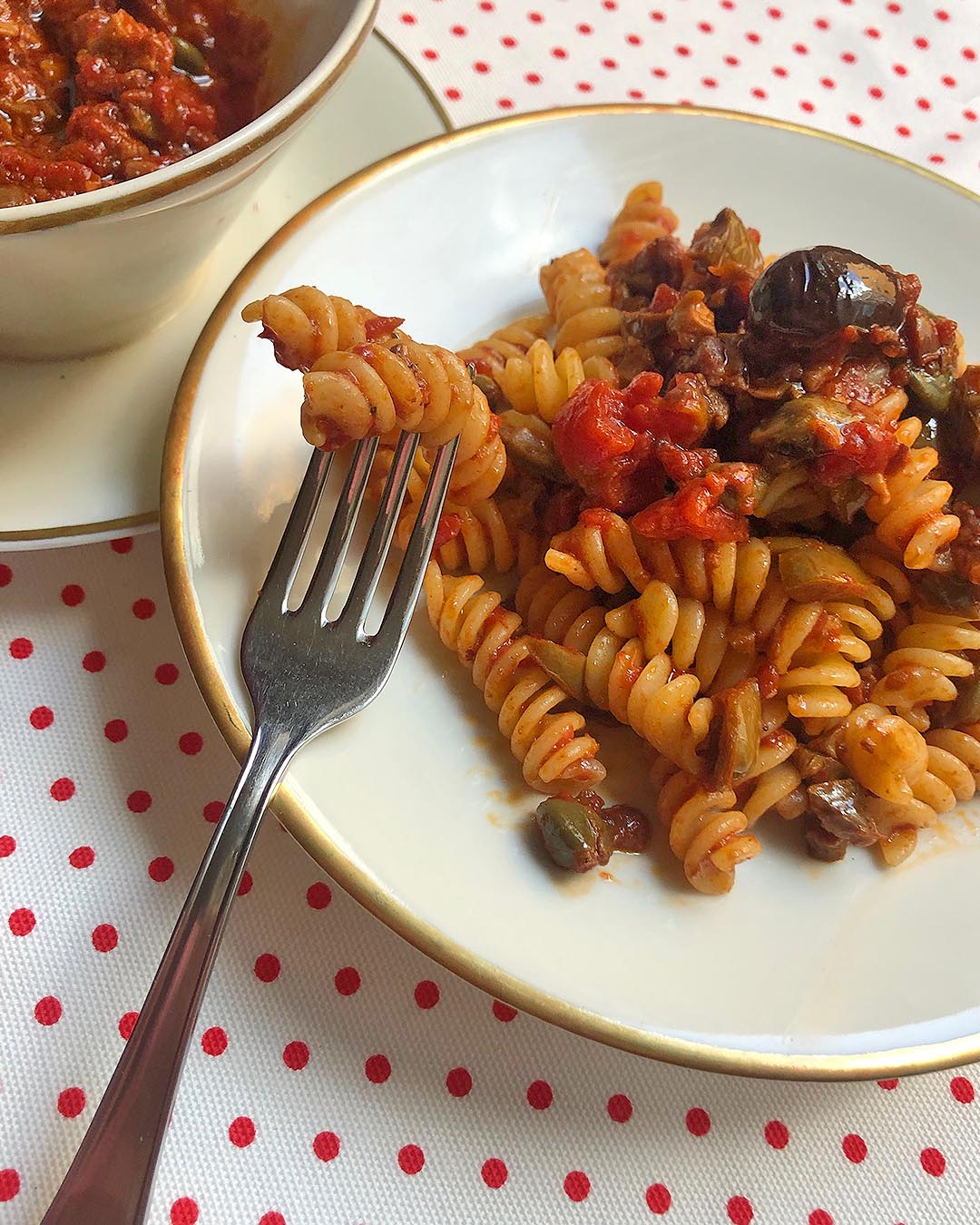 fusilli alla puttanesca served on a white dish with sauce on a side